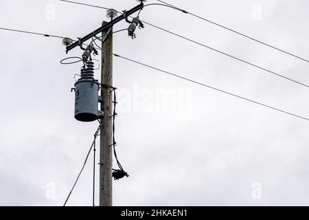 Externer Transformator, der an einer hölzernen Stromhalterung in elektrische Energie aufgehängt ist Stockfoto