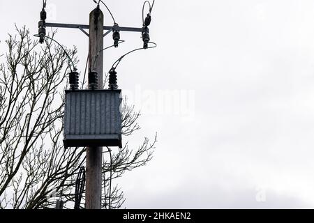 Externer Transformator, der an einer hölzernen Stromhalterung in elektrische Energie aufgehängt ist Stockfoto