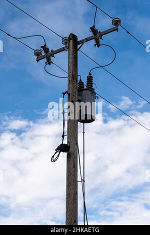 Externer Transformator, der an einer hölzernen Stromhalterung in elektrische Energie aufgehängt ist Stockfoto