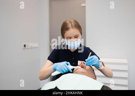 Ärztin Zahnärztin verwendet ultraviolette Lampe, während die Zähne des männlichen Patienten gefüllt werden Stockfoto