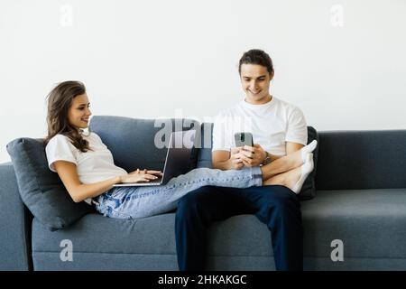 Liebenswert Paar Mann und Frau im Wohnzimmer ruhen und mit Laptop-Computer und Smartphone mit einem Lächeln Stockfoto