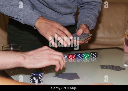 Man's Hands shuffling Karten in einem Poker-Spiel. Chips, Karten, ein Glas Champagner auf dem Tisch mit Spiegelung. Poker Club. Stockfoto