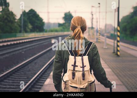 Frau, die am Bahnhof auf den Zug wartet. Tourist mit Rucksack, der bei Regen auf dem Bahnsteig steht Stockfoto