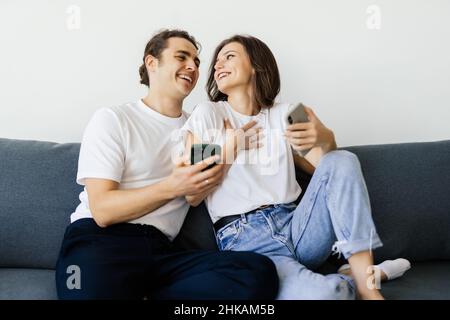 Mobile Suchtkonzept, junges Paar mit Smartphones auf dem Sofa entspannen, Millennial Mann und Frau besessen von neuen Apps oder sozialen Netzwerken, Telefon A Stockfoto