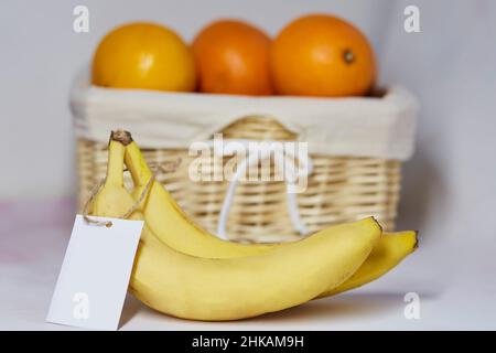 Mock-up-Etikett auf Bananen. Aufkleber Produkt für Text oder Preis. Korb mit Orangen auf dem Hintergrund. Bio-Landwirtschaftsprodukte vom lokalen Markt. Speicherplatz kopieren Stockfoto