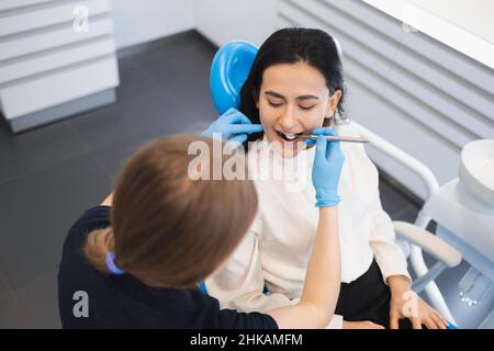 Bild einer hübschen jungen Frau, die im Zahnarztstuhl im medizinischen Zentrum sitzt, während ein professioneller Arzt ihre Zähne überprüft Stockfoto