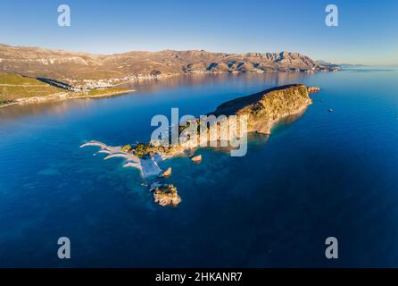 Luftaufnahme von Sveti Nikola, Budva Insel, Montenegro. Hawaii Strand, Sonnenschirme und Badegäste und kristallklares Wasser. Zerklüftete Küsten mit schroffen Klippen Stockfoto