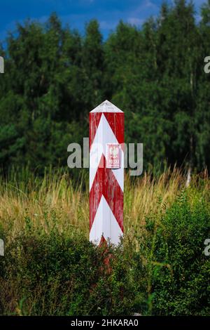 Hölzerner rot-weiß polnischer Grenzposten mit Emblem auf Platte steht auf Wiese mit Gras Stockfoto