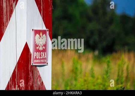 Hölzerner rot-weiß polnischer Grenzposten mit Emblem auf Platte steht auf Wiese mit Gras Stockfoto