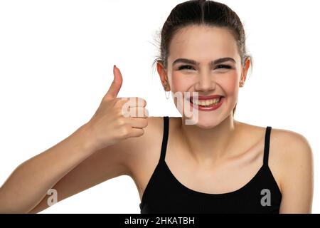 Porträt eines glücklichen Teenagers mit gebundenem Haar, der den Daumen auf einem weißen Hintergrund zeigt Stockfoto