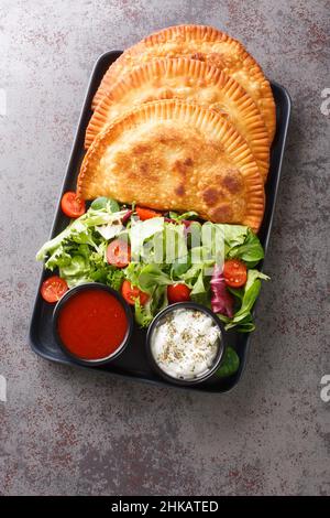 Traditionelle russische frittierte Fleischpasteten Chebureki mit frischem Salat und Saucen in der Nähe auf einem Teller auf dem Tisch. Vertikale Draufsicht von oben Stockfoto