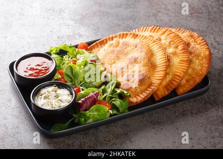 Chebureki ist ein Gericht der krimtatarischen Küche, das mit frischem Salat und Saucen aus der Nähe auf einem Teller auf dem Tisch serviert wird. Horizontal Stockfoto