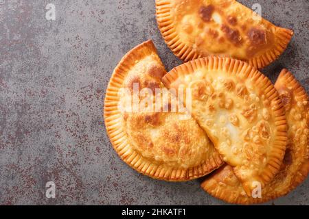 Cheburek wird aus ungesäuertem Teig hergestellt, der mit gemahlenem Fleisch, Zwiebeln und Gewürzen gefüllt ist, die in Öl in der Nähe auf dem Tisch gebraten werden. Horizontale Draufsicht von oben Stockfoto