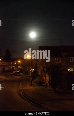 An einem dunklen Winterabend scheint ein trüblicher Mond auf eine englische Straße herab Stockfoto