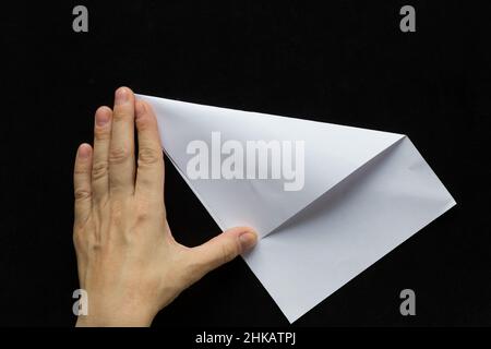 Frau Hände Falten rechteckigen Blatt Papier, um es quadratisch auf schwarzem Hintergrund zu machen Stockfoto