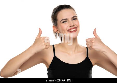 Porträt eines lächelnden Teenagers mit gefesselten Haaren, die Daumen nach oben auf weißem Hintergrund zeigen Stockfoto