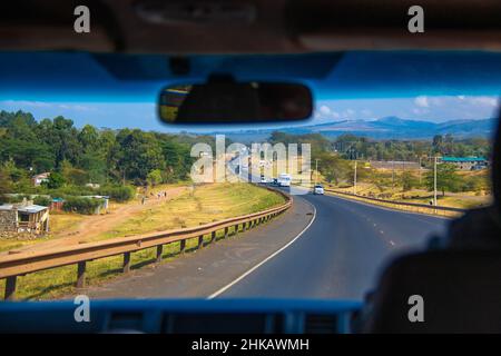 Blick vom Fahrer auf das Landkap, vorbei an einem Dorf auf einer kenianischen Autobahn durch das Great Rift Valley westlich von Nairobi, Kenia Stockfoto