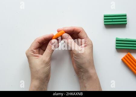 Frau Hände machen kleine Karotten Fimo auf dem weißen Hintergrund Stockfoto