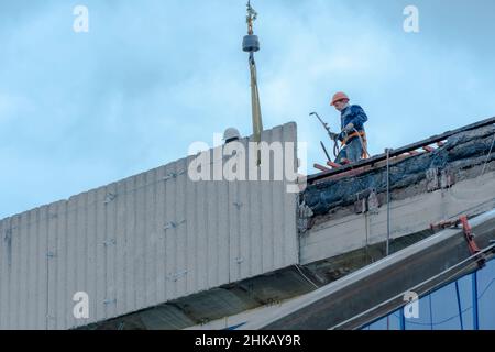 Moskau,Russland,05,10,2021:Restaurierung,Rekonstruktion und Reparatur des Gebäudes.Bauarbeiter in Harthüten installieren Betonplatten auf dem Dach des Gebäudes Stockfoto