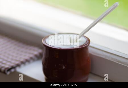 Frischer Joghurt in einem braunen Tontopf auf der Fensterbank Stockfoto