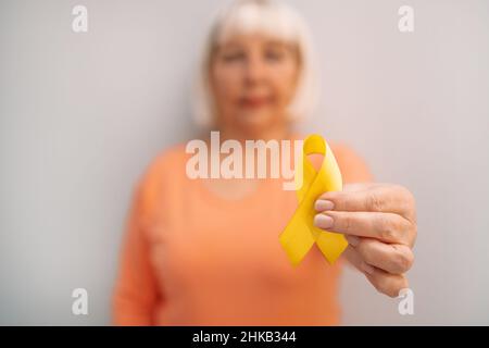 Frau Hand hält gelbe Band Symbol der Kindheit Krebs Bewusstsein Monat auf grauem Hintergrund mit Copy Space Stockfoto