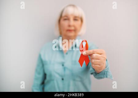 Weibliche Hand mit rotem Band auf grauem Hintergrund, hiv-Bewusstseinskonzept, Welt-Aids-Tag, Welt-Hypertonie-Tag Stockfoto