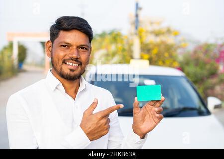 Lächelnder Taxifahrer zeigt leere Karte, indem er die Kamera vor dem Auto anschaut - Konzept eines personalausweises, Werbung und Werbeaktionen. Stockfoto