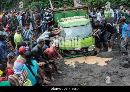 Yogyakarta, Indonesien. 3rd. Februar 2022. Menschen versuchen, Fahrzeuge, die in Materialien aus kalter Lava vom Berg Merapi am Boyong River im Bezirk Sleman, Yogyakarta, Indonesien, gefangen sind, zu evakuieren, 3. Februar 2022. Starke Regenfälle um den Hang des Mount Merapi am Donnerstag verursachten einen Erdrutsch der vulkanischen Lagerstätte am Boyong River. Es wurden keine Verletzten gemeldet. Quelle: Priyo Utomo/Xinhua/Alamy Live News Stockfoto