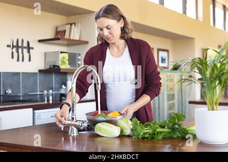 Kaukasische Schwangerin, die Gemüse in der Spüle in der Küche zu Hause wäscht Stockfoto