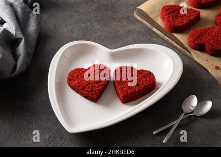 Herzzonierte rote Samtkuchen für zwei zum Valentinstag auf dunklem Hintergrund. Leckeres hausgemachtes Dessert. Nahaufnahme. Stockfoto