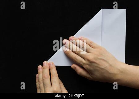 Frau Hände Falten rechteckigen Blatt Papier, um es quadratisch auf schwarzem Hintergrund zu machen Stockfoto