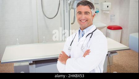 Porträt eines lächelnden kaukasischen reifen männlichen Arztes mit gekreuzten Armen, der auf der Krankenstation steht Stockfoto