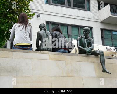 Eine Gruppe von Bronzefiguren und zwei jungen Frauen an der Uferpromenade der Spree in Berlin. Stockfoto