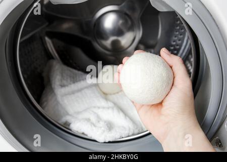 Frau, die Wolltrocknerkugeln für weichere Kleidung verwendet, während sie im Waschmaschinenkonzept trocknet. Entladen Sie statische Elektrizität und verkürzen Sie die Trocknung. Stockfoto