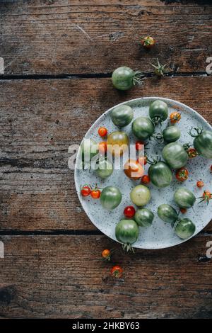 Ein Teller mit kleinen grünen und roten Tomaten auf einem Holztisch Stockfoto