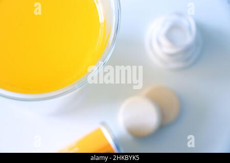 Vitamin C-Getränk im Vordergrund, Vitamin C lösbare Tabletten aus der Tube auf einem weißen Tisch im Hintergrund, selektiver Fokus Stockfoto