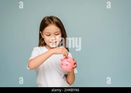 Ein kleines Mädchen steckt eine Münze in ein Sparschwein. Das Konzept, Kindern persönliche Finanzen und Sparen beizubringen Stockfoto