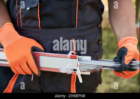 Nahaufnahme von Menschenhänden in Arbeitshandschuhen mit Schweißelektroden. Männlicher Baumeister mit beschichteten Metalldrähten oder Schweißstäben klebt in den Händen. Stockfoto