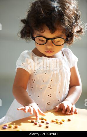 Medikamente haben viele Verwendungen. Aufnahme eines kleinen Mädchens zu Hause allein mit Pillen auf dem Tisch vor ihr. Stockfoto