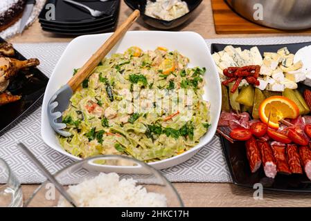 Grüne Tagliatelle in Gorgonzola-Sauce, die auf einem weißen Teller mit einem Holzlöffel auf einem mit Lebensmitteln gefüllten Tisch liegt. Stockfoto