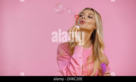 Blonde Frau hält Zauberstab während Seifenblasen isoliert auf rosa Stockfoto