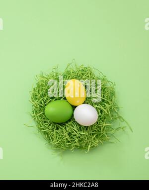 Ostereier im Nest, pastellgrüner Hintergrund, Draufsicht. Frühlingsfeiertage, Platz kopieren. Stockfoto