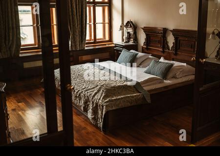 Stilvolles mittelalterliches antikes europäisches, schickes Hotelzimmer mit Holzboden und Bett mit grünen Kissen, Laken, Bettüberwurf und Zimmerlampe im Hintergrund. Stockfoto