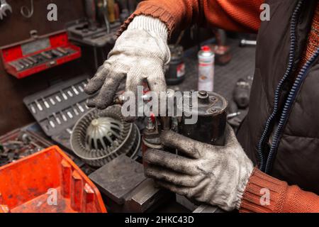 Mechaniker mit schmutzigen Handschuhen reparieren gebrochenen Anlasser am Auto. Kfz-Service. Stockfoto