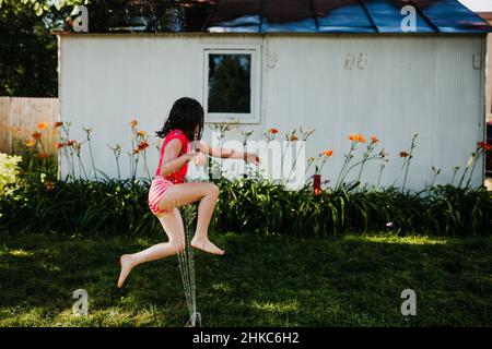 Im Sommer läuft das junge Mädchen durch den Sprinkler im Hinterhof Stockfoto