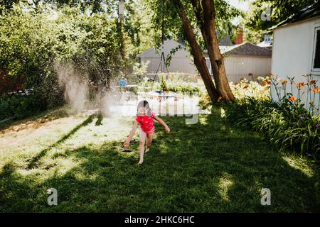 Im Sommer läuft das junge Mädchen durch den Sprinkler im Hinterhof Stockfoto