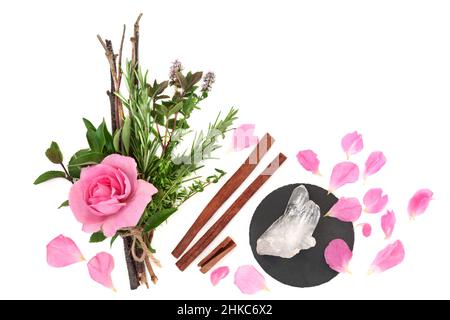 Liebestrank-Kräuter, gebunden in einem Hexenbündel mit rosa Rosenblüten, losen Blütenblättern, Zimt-Gewürzen und Quarzkristall auf Weiß. Pagan Magic Spell Konzept. Stockfoto