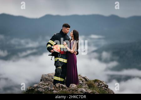 Glücklicher Feuerwehrmann umarmt seine Frau in den Bergen Stockfoto