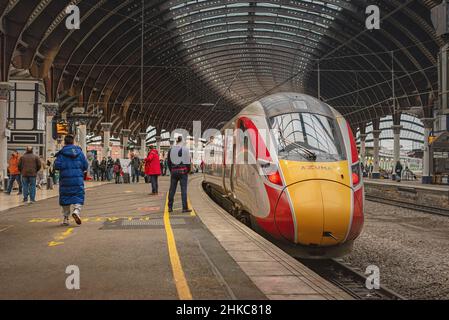 Bahnhofsplatz mit einem Zug daneben. Oben ist ein historisches Vordach mit Säulen und Passagiere sind auf dem Bahnsteig. Stockfoto