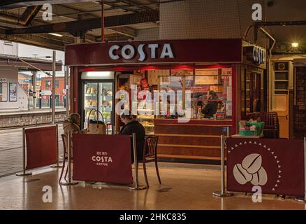 Ein Kiosk, der Kaffee verkauft, in einer Unterführung eines Bahnhofs. Zwei Personen sitzen an einem Tisch und eine Plattform befindet sich in der Ferne. Stockfoto